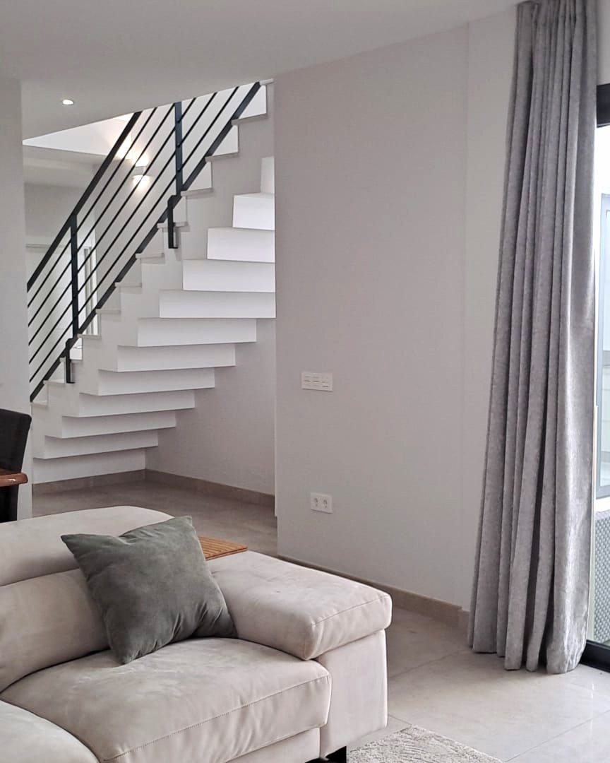 Salón de vivienda unifamiliar con escalera de peldaños en voladizo y barandilla metálica, obra de CAC Arquitectos